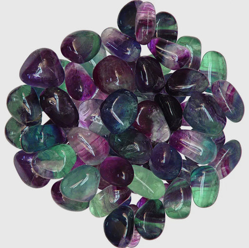 A close-up of tumbled fluorite with shades of purple, blue, and green.